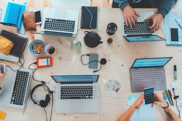 Birdseye of open laptops from 5 cybersecurity professionals around a table