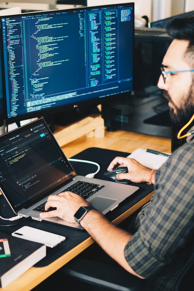 Cybersecurity professional man at desk with open laptop and large monitor