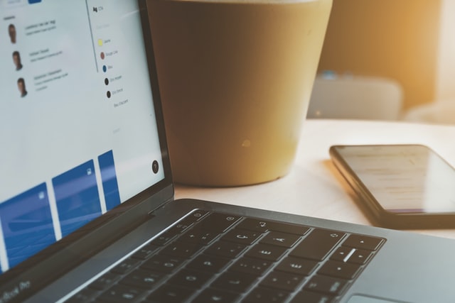 Corner of open laptop screen and keyboard with cellphone at desk