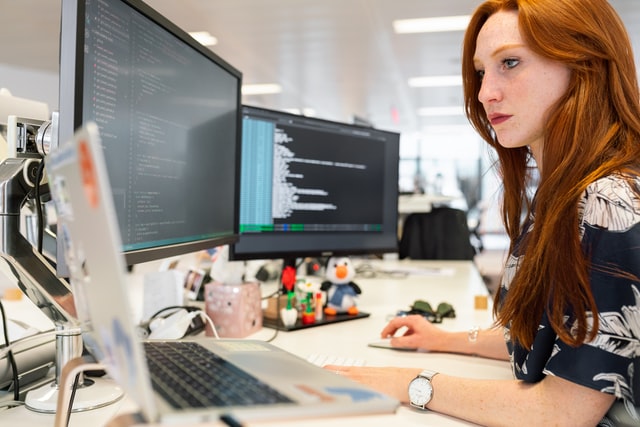 Cybersecurity professional woman at desk with open laptop and large monitor